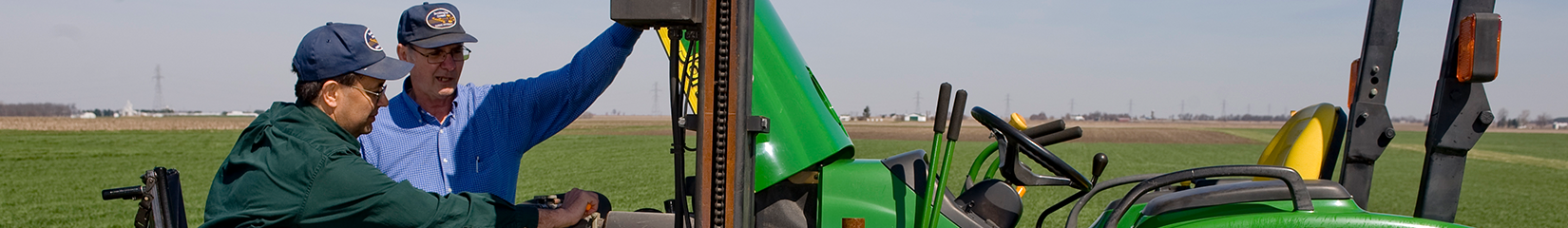 A photo of two people in a field where one is mounted on a tractor using their mobility device.